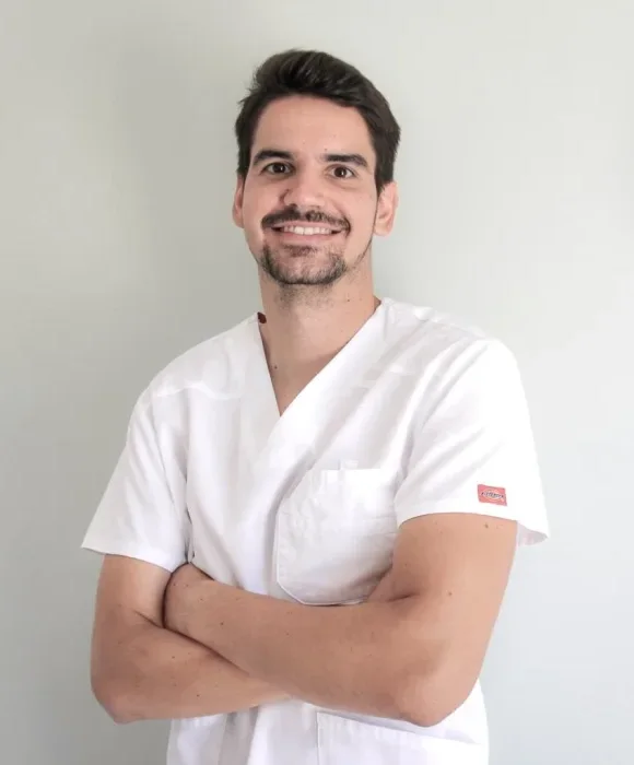 Nicolas Roques, ostéopathe D.O., souriant en blouse blanche, bras croisés